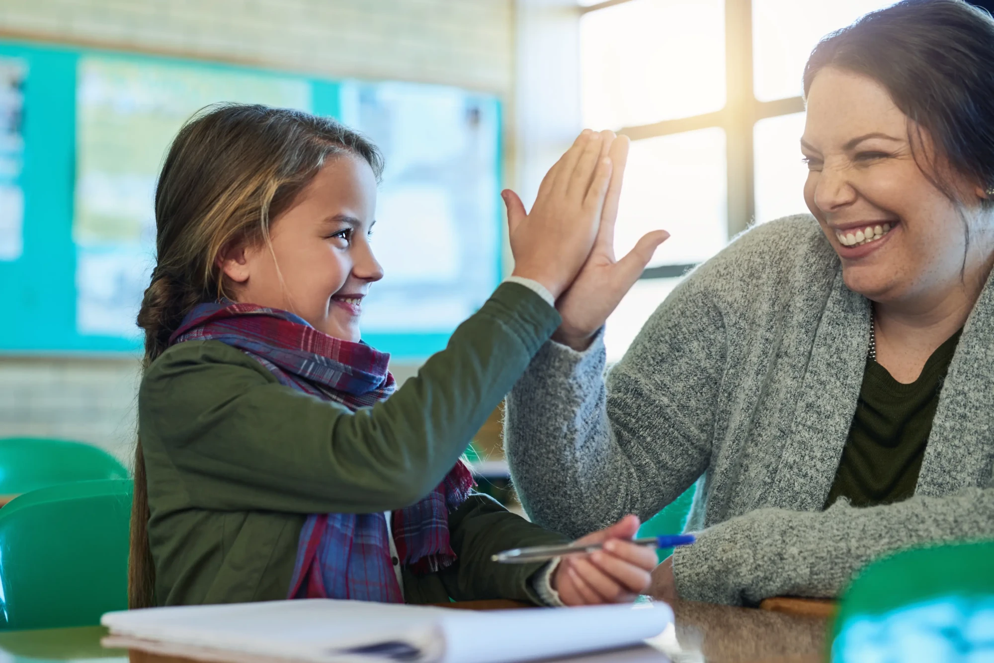 high-five-student-teacher-happy-help-with-work-study-learning-math-classroom-girl-education-book-pen-child-success-achievement-school-helping-woman-support